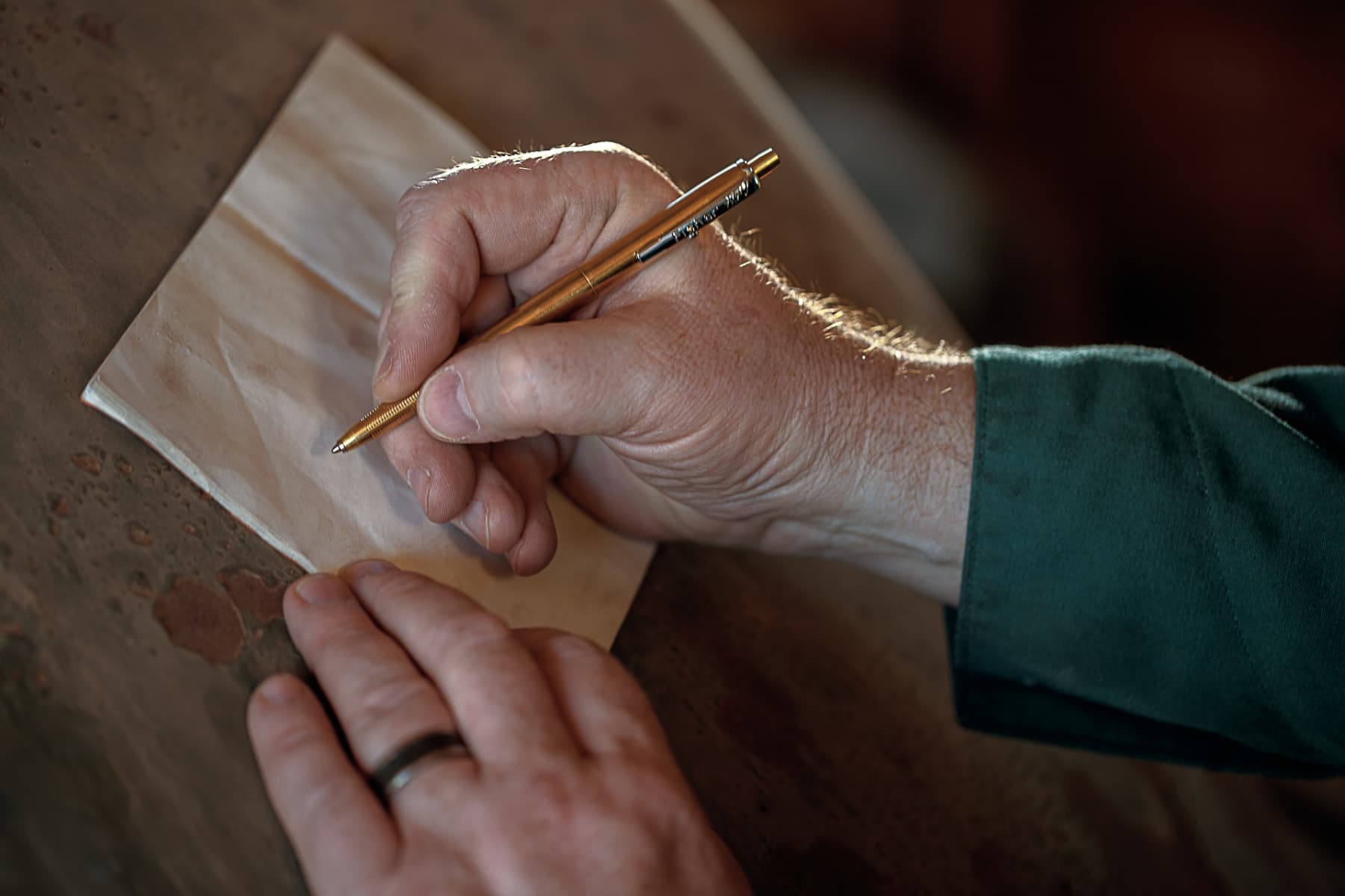 Close-up of a person writing with a raw brass AG7 Fisher Space Pen on a sheet of paper