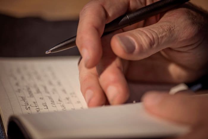 Hand holding an open 400B matte black bullet space pen over a lined notebook with writing in it.
