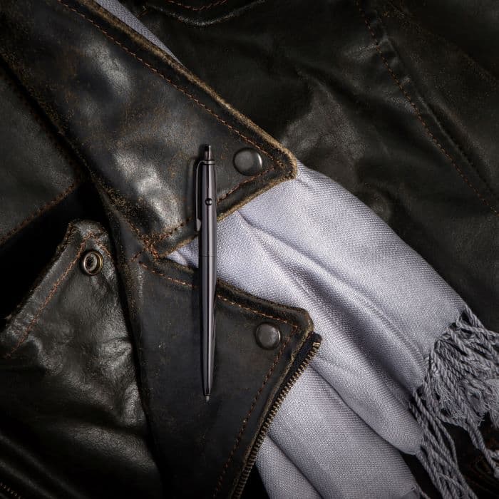 AG7-BTN Dark Matter Astronaut Space Pen in black titanium nitride  laying atop the lapel of a leather jacket and a silver knit scarf with fringe.