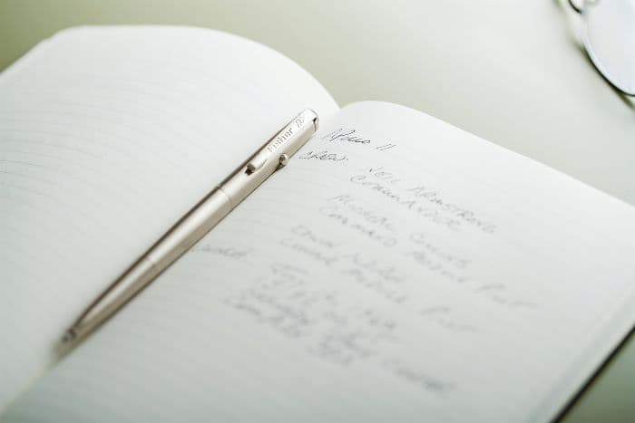 AG7-MW Moonwalker Nickel Titanium Nitride Astronaut Space Pen laying atopan open lined notebook with handwriting.